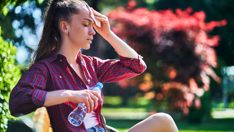 A woman wiping her forehead whilst sat in the sun